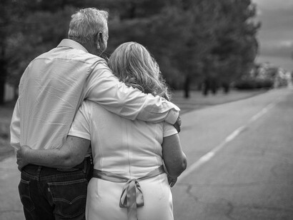 An elderly couple embrace and walk on an autumn road