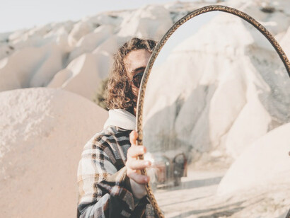In the vast desert, a man stood, holding a mirror, exemplifying the interconnectedness of different levels or aspects of reality as he reflected the shimmering sunlight onto the distant mountains