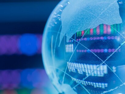 A shining crystal globe with stock market visuals on a computer screen in the background, reflecting the dynamics of global economies