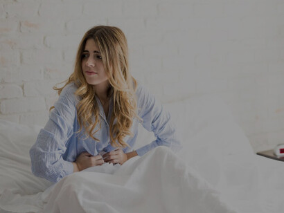 Woman in comfortable sleepwear struggling with menstrual cramps in bed, illustrating the challenges of managing menstrual pain