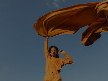 Embodiment of liberation and authenticity, captured in the serene image of a woman holding a yellow cloth amidst nature's beauty