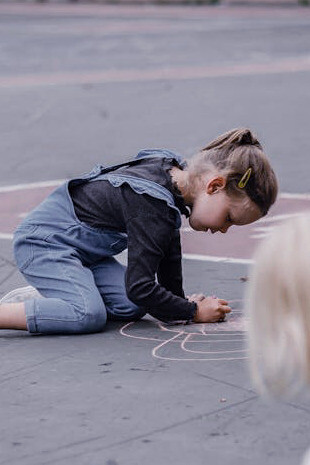 With each chalk stroke, the young girl brings to life the classic hopscotch grid, evoking the same excitement and determination that defined countless childhood games
