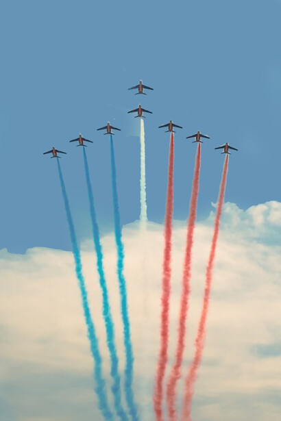 Aircraft in mid-flight, streaking across the sky with contrails of blue, red, and white, soaring above the Circuit Le Mans in Le Mans, France