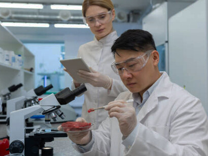 A male scientist carefully studies lab-grown meat, while his colleagues perform experiments in the background, pushing the boundaries of cultured meat production and artificial food innovation