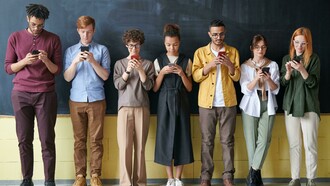 A group of people stands near a blackboard, each focused on their phones instead of the board