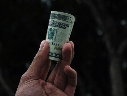 In a person's hand, a stack of dollar bills is held tightly, the edges of the notes peeking out