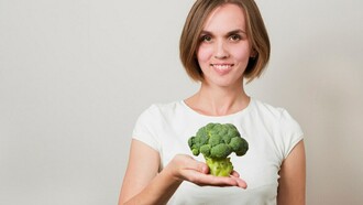 A woman holding a fresh broccoli, emphasizing healthy plant-based nutrition