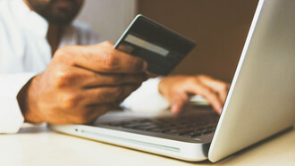 A man holding a credit card in front of his laptop