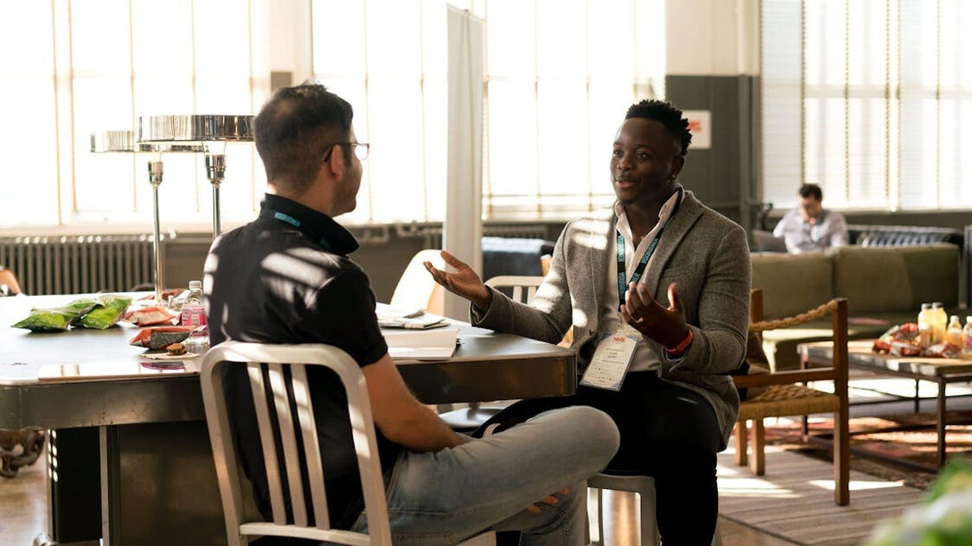 Two men engage in a deep conversation, pondering the complexities of merit and achievement, as they navigate the challenges of imposter syndrome and the deserving threshold