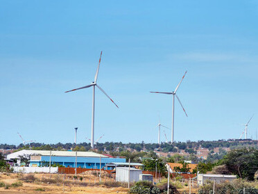 Windmills stand tall against the backdrop of trees and buildings in the serene countryside of the UK, blending traditional rural charm with modern renewable energy