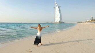 A woman walks along the seashore toward the Burj Al Arab in Dubai, United Arab Emirates