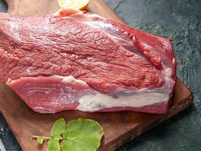 Fresh raw red meat displayed on a wooden cutting board with a nude-colored towel, lemon, and garlic, against a vibrant, mixed-color background