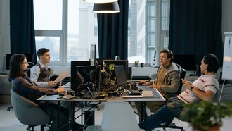 Quatro homens trabalham em frente a computadores num ambiente de escritório. A baixa diversidade nas equipas que desenvolvem inteligência artificial é apontada por especialistas como um dos fatores que contribuem para pontos cegos e vieses nos sistemas. O artigo discute como as escolhas de quem cria a IA influenciam os resultados produzidos pelos algoritmos. A predominância masculina em áreas ligadas à inteligência artificial continua a ser um desafio para a diversidade de perspectivas no setor