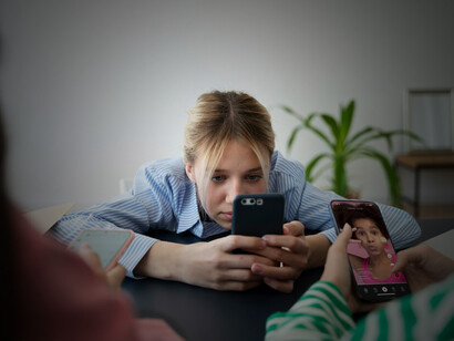 A young woman staring at her smartphone with a downcast expression, symbolizing the toll of social media on self-esteem and the isolation brought on by online comparisons
