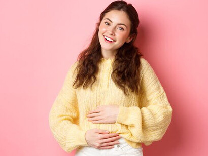 Joyful young woman with a relieved expression, touching her stomach, showcasing the benefits of improved gut health through colon cleansing, hormone-boosting foods, and probiotics