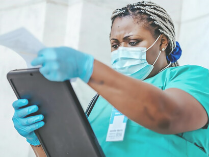 A proficient doctor, donned in a mask, attentively reviews the medical chart in her grasp