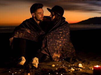 Young couple wrapped in a blanket, sharing a romantic moment on the sea shore, epitomizing love and relationship