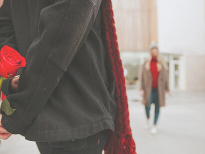 An unrecognizable man holds a red rose, waiting for a woman