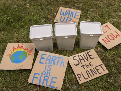 Several signs pleading for climate action beside recycling bins