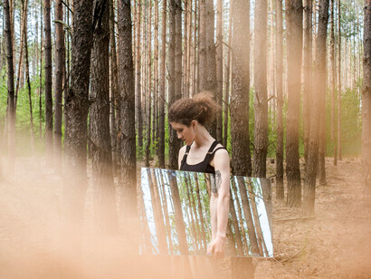 A woman holds a mirror in a forest