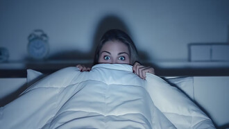 A woman, wrapped in a blanket, enjoying a horror movie with a frightened expression