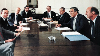 Reunião de diretoria do S.G. Warburg & Co., um influente banco de investimento britânico, por volta de 1980. Warburg foi fundamental na criação do mercado de Eurobonds e era famoso por sua cultura de trabalho intensa, muitas vezes descrita como quase monástica em comparação com outros bancos da época