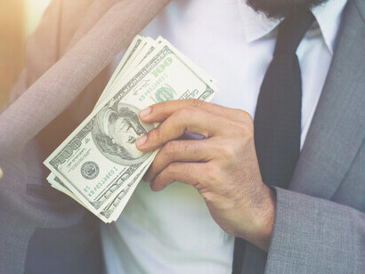 A man in a suit clandestinely pockets cash, emblematic of corruption