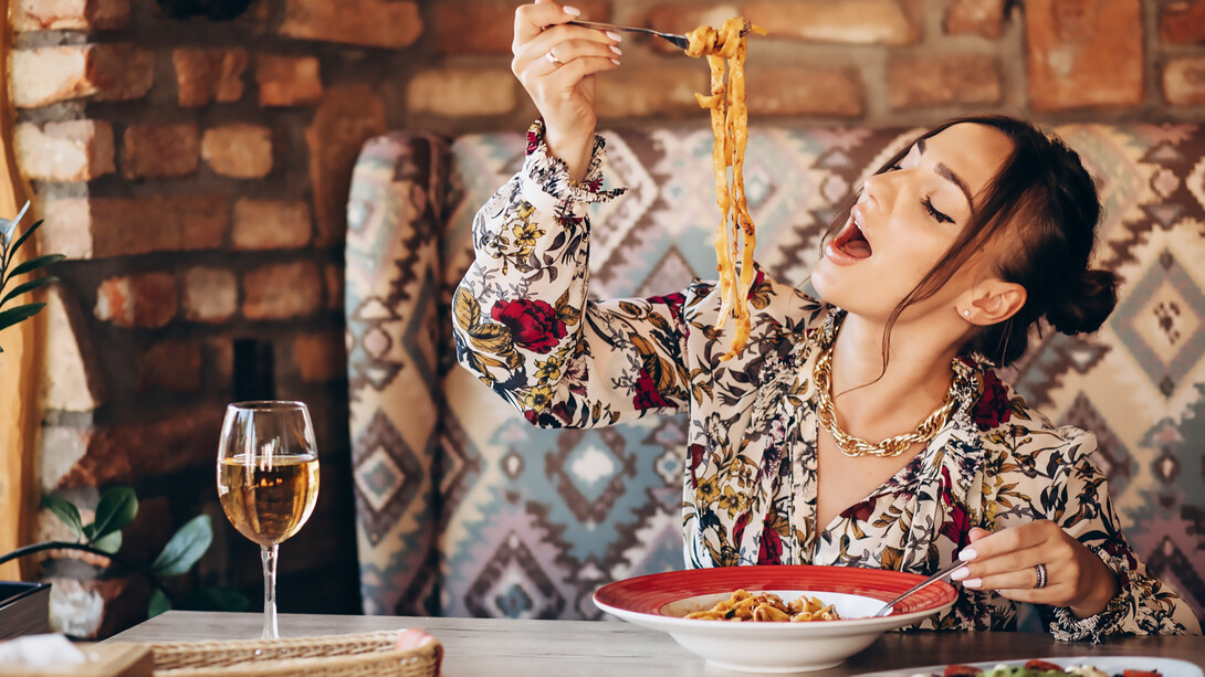 A woman savors delicious pasta in a cozy Italian restaurant, immersing in the ambiance of traditional dining