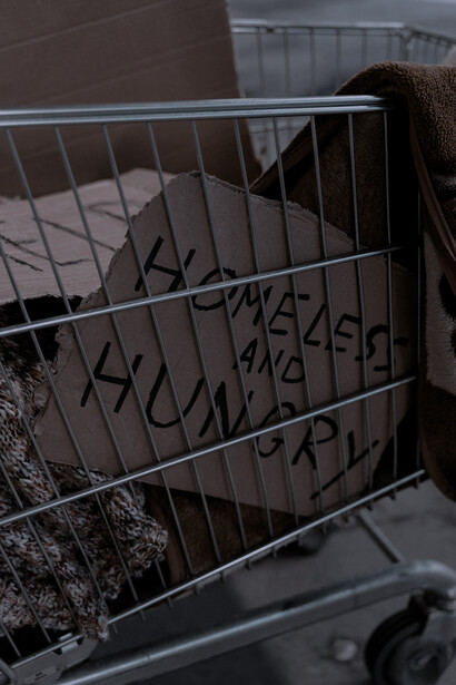 Shopping cart, with a sign that reads: homeless and hungry. Social sustainability focuses on how the requirements of the people are being met