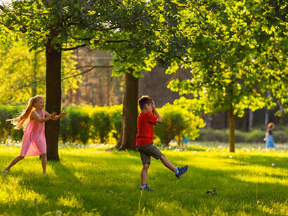 Young kids playing with a red ball on the green grass of a park on a summer day