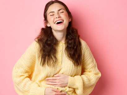 Young, smiling woman feeling relieved and happy, touching her stomach to highlight improved gut health with colon cleansing, hormone-boosting foods, and probiotic-rich diet