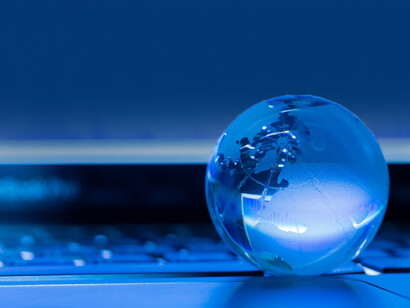 A crystal globe placed in front of a computer screen displaying stock market data, symbolizing global economies