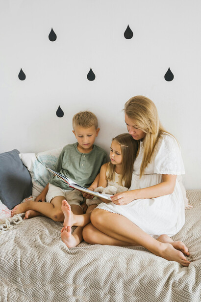 Mãe lendo e ensinando linguagem para seus filhos reflete a transmissão de conhecimento e valores através da interação verbal, fundamental para o desenvolvimento humano