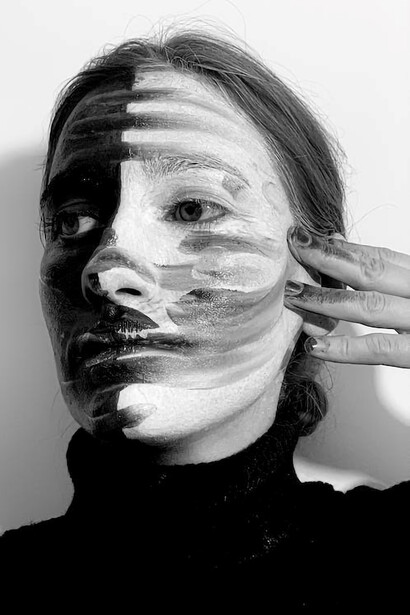 Her visage tells a powerful story as one half is painted in deep black and the other in pristine white, capturing the profound disconnection she experiences