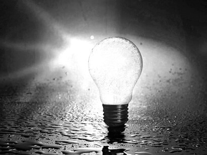 A glowing lightbulb that is surrounded by small puddles of water and still producing energy