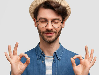 A brunet man in a denim shirt and hat, crossing his fingers, letting go of expectations and embracing the art of surrender captured in this evocative image