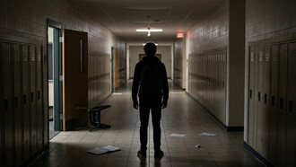 A student standing silently in a dimly lit school hallway, reflecting the importance of mental health and early intervention