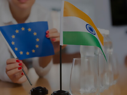 Delegation employee prepares the negotiating table, arranging flags of the European Union and India, symbolizing diplomatic discussions and collaboration between nations