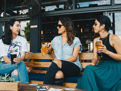 Three women drink a beer at a bar, conversing
