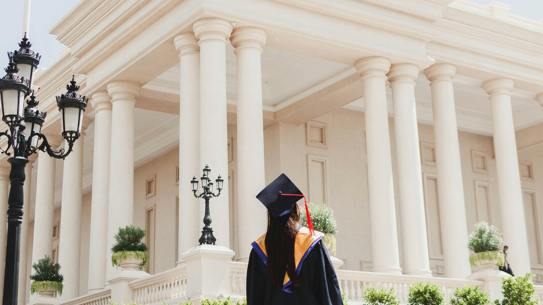 A woman in an academic robe looking at an imposing building