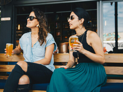 Two young women in sunglasses drinking a beer at a bar