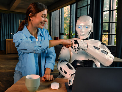 Human employee and humanoid robot working together at a laptop in a collaborative workplace