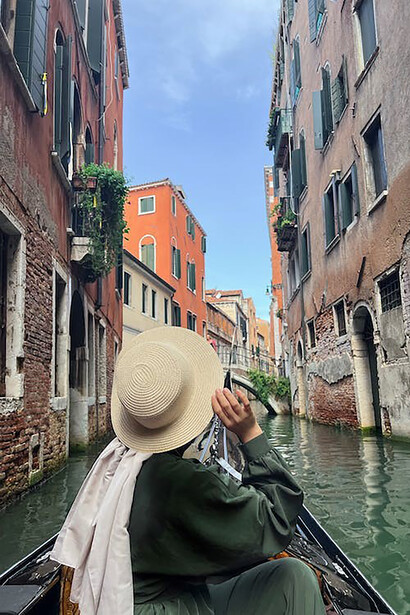 Amidst her expat journey, a woman in a gondola embraces the beauty of Venice, Italy, as she navigates the enchanting waterways