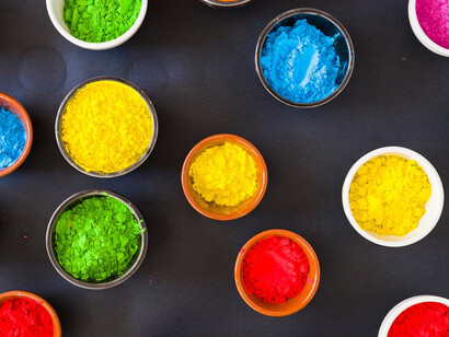 An overhead view of bowls filled with vibrant Holi powder on a black backdrop highlights the interplay of color psychology