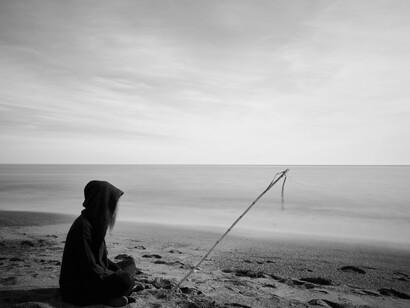 A figure in black with a fishing pole, sitting on the bech