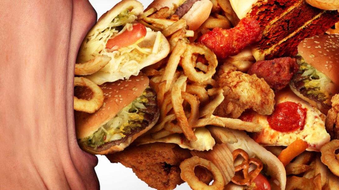 A man opens his mouth wide to over eat a lot of junk food