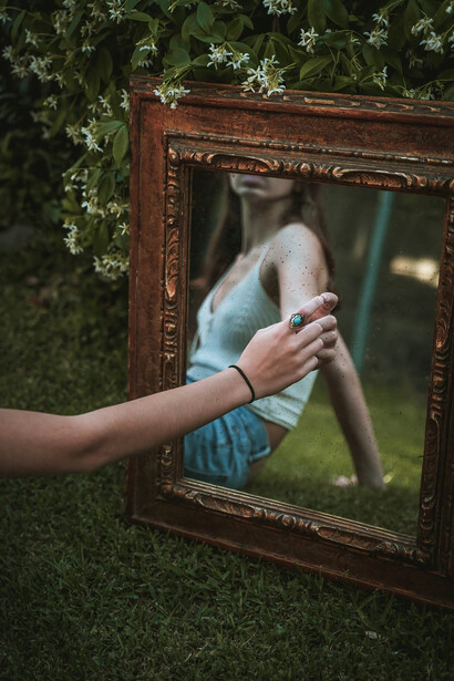 A person holds a weathered brown wooden frame, within which a reflection captures an aura of antiquity and age, evoking a sense of ancient times and old-world charm