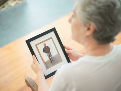 Back view of an elderly woman holding a black picture frame, expressing grief and remembrance