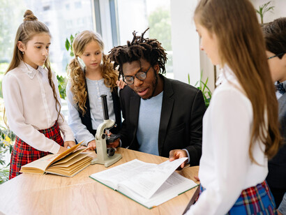 Children and their teacher in a classroom with a microscope