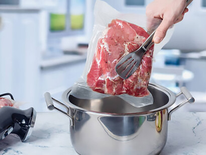 Alarming reliance on plastic as a woman deposits vacuum-sealed meat into a pot with a sous vide cooker, underscoring the negative consequences of excessive plastic usage in kitchen routines